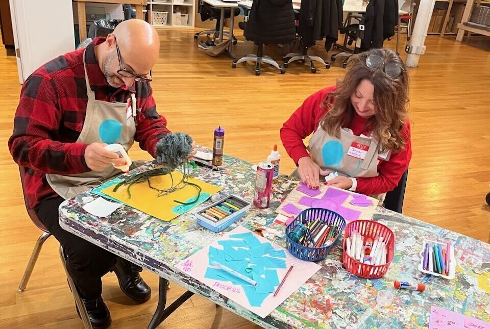 Man and woman applying mixed media to paper with glue while sitting at a craft table