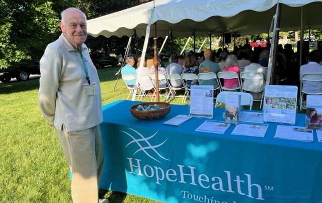 Man standing in front of a table with brochures and a teal tablecloth that says HopeHealth