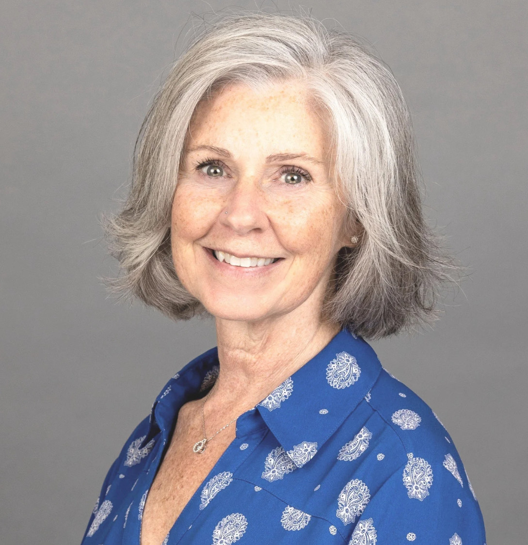 Woman with blue button down shirt and short haircut smiles for her photo as she volunteers with hospice patients