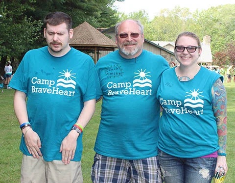 Dad in the middle with adult kids on either side of him wearing teal Camp BraveHeart shirts