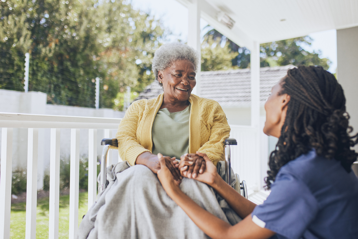 Young female nurse holding hands with an elderly patient in a wheelchair. Concept of assisted living at a nursing home.