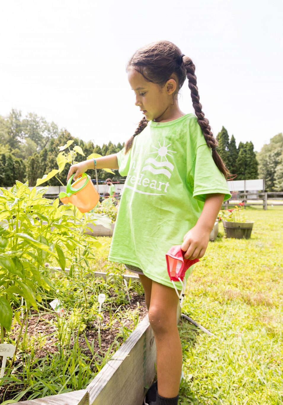 Camp BraveHeart 2021 Little girl in pigtail braids watering plants at Camp BraveHeart