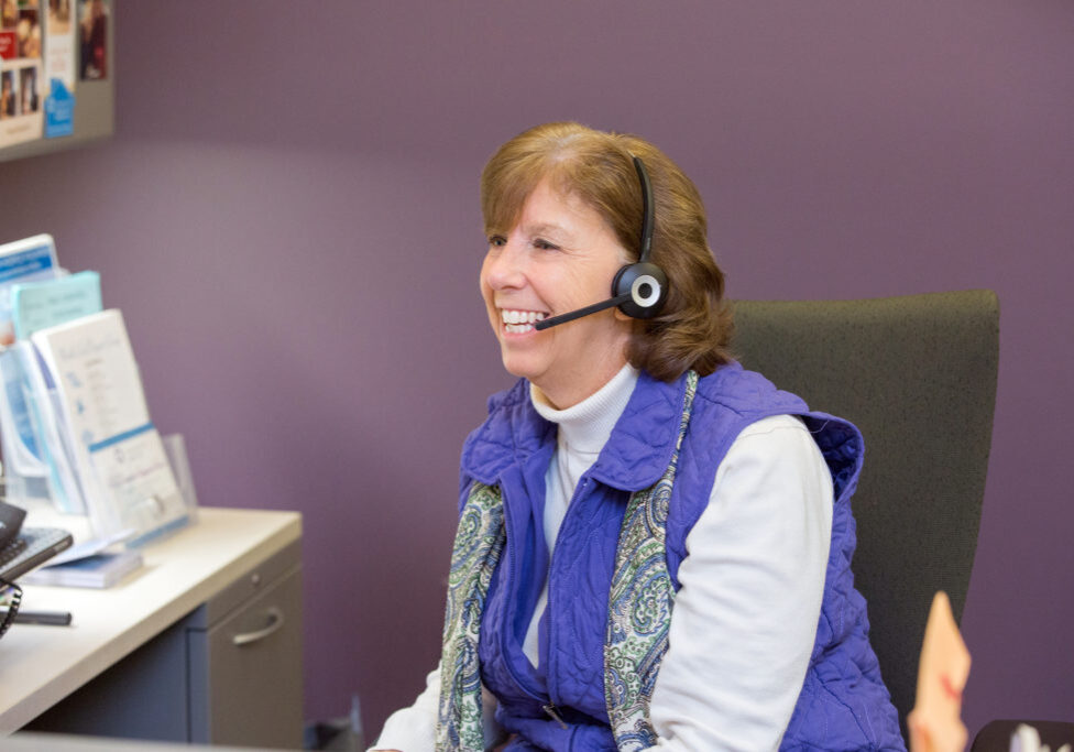 head and torso of woman at computer wearing headset with a purple wall