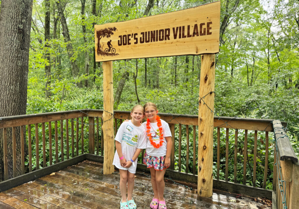 Two young girls stand under a sign that reads "Joe's Junior Village"