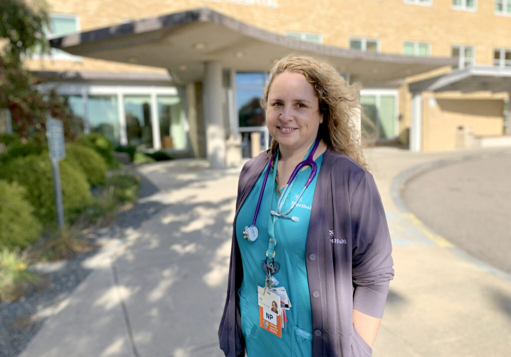 Woman in hospital scrubs stands uotside hospital entrance