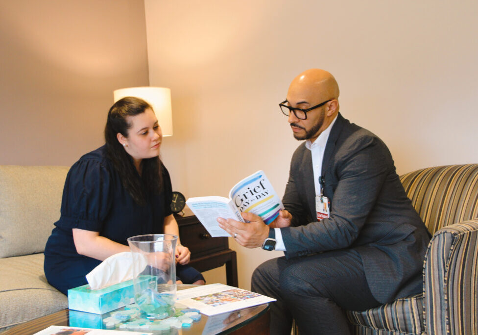 Man and woman sitting on chairs next to each other reading a book on grief support