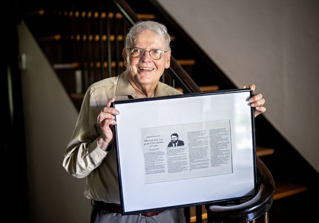 Man stands in stairwell holding a framed news story