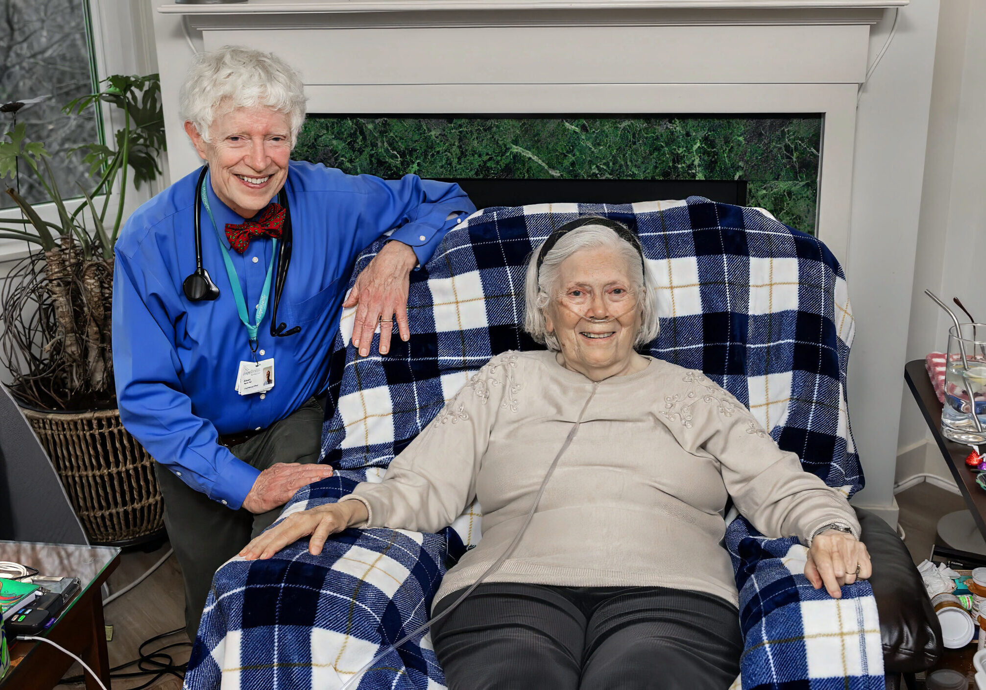 A doctor sits next to a hospice patient sitting in their chair smiling