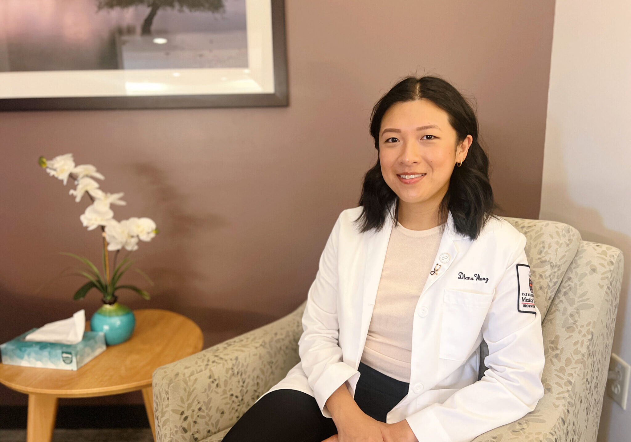 Brown University medical student sitting in chair next to a table with a plant and tissues