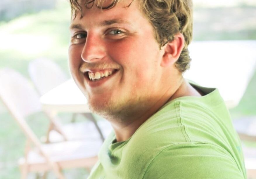 Young male with blond hair and blue eyes, wearing a green shirt and smiling