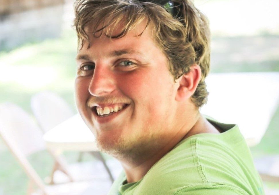 Young male with blond hair and blue eyes, wearing a green shirt and smiling