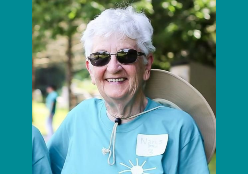 Elderly woman with white hair wearing sunglasses and a hat around her neck