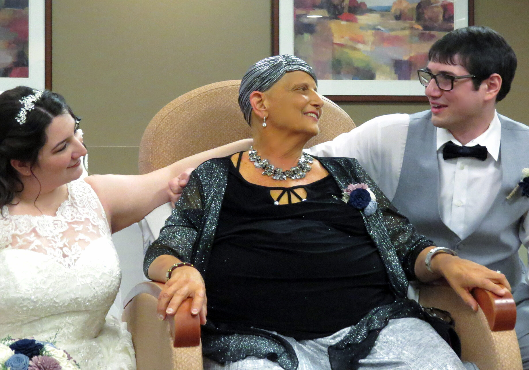 Woman on hospice service looks at her son as his bride sits to the left of her