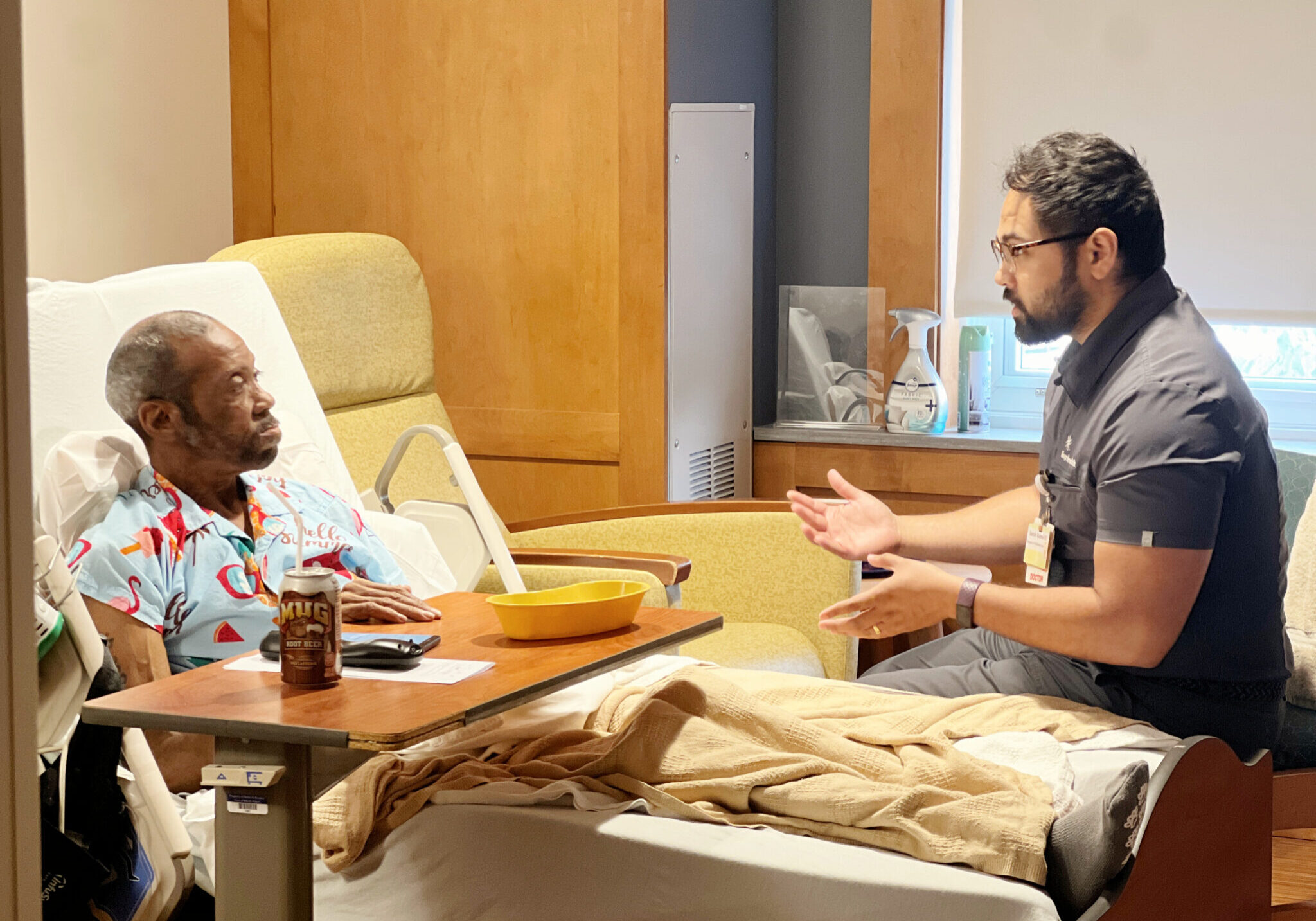 A patient sits in his hospice bed, talking to his doctor