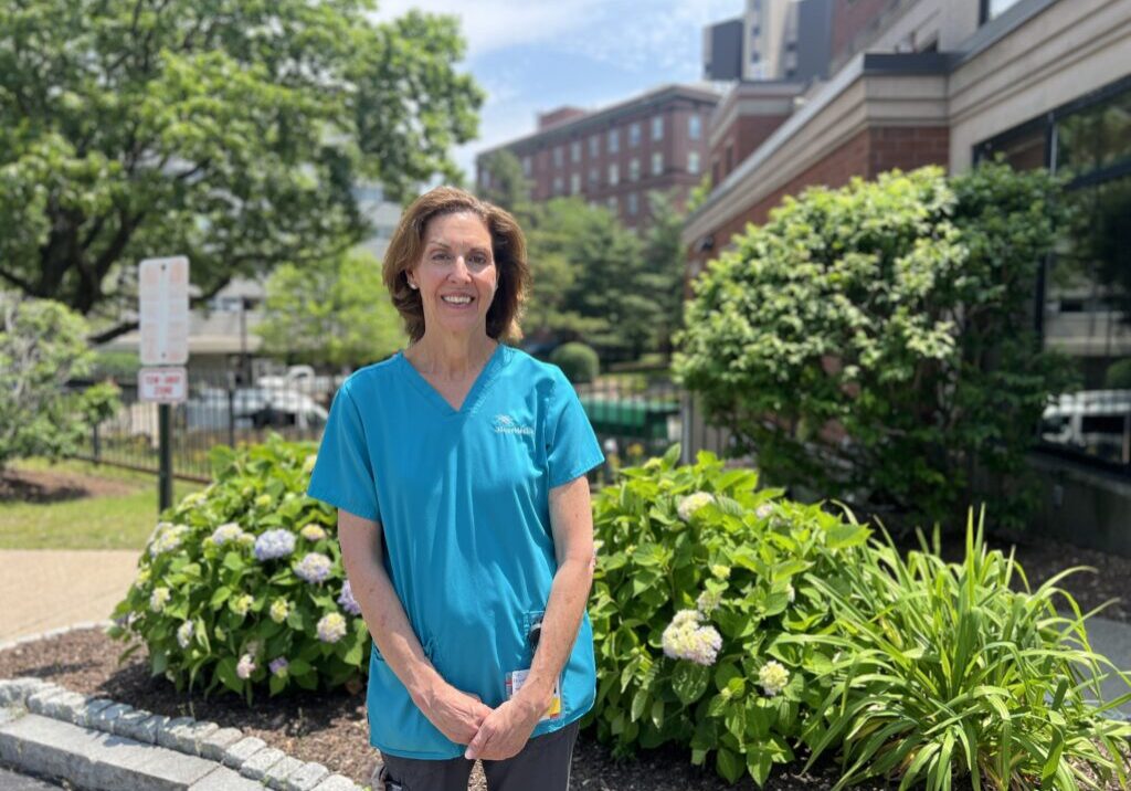 IMG_7952 Female hospice aide standing in front of hydrangea bushes and brick buildings