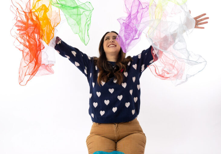 Dance/Movement Therapist for PediPal Services throws colorful fabric in the air, against a white background