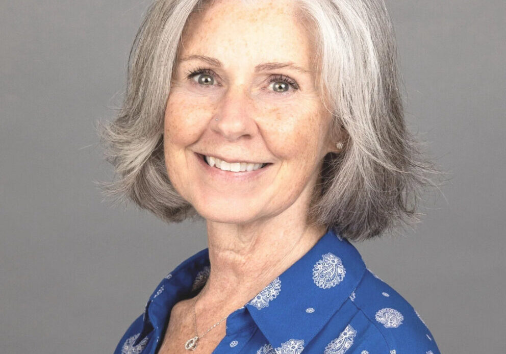 Woman with blue button down shirt and short haircut smiles for her photo as she volunteers with hospice patients
