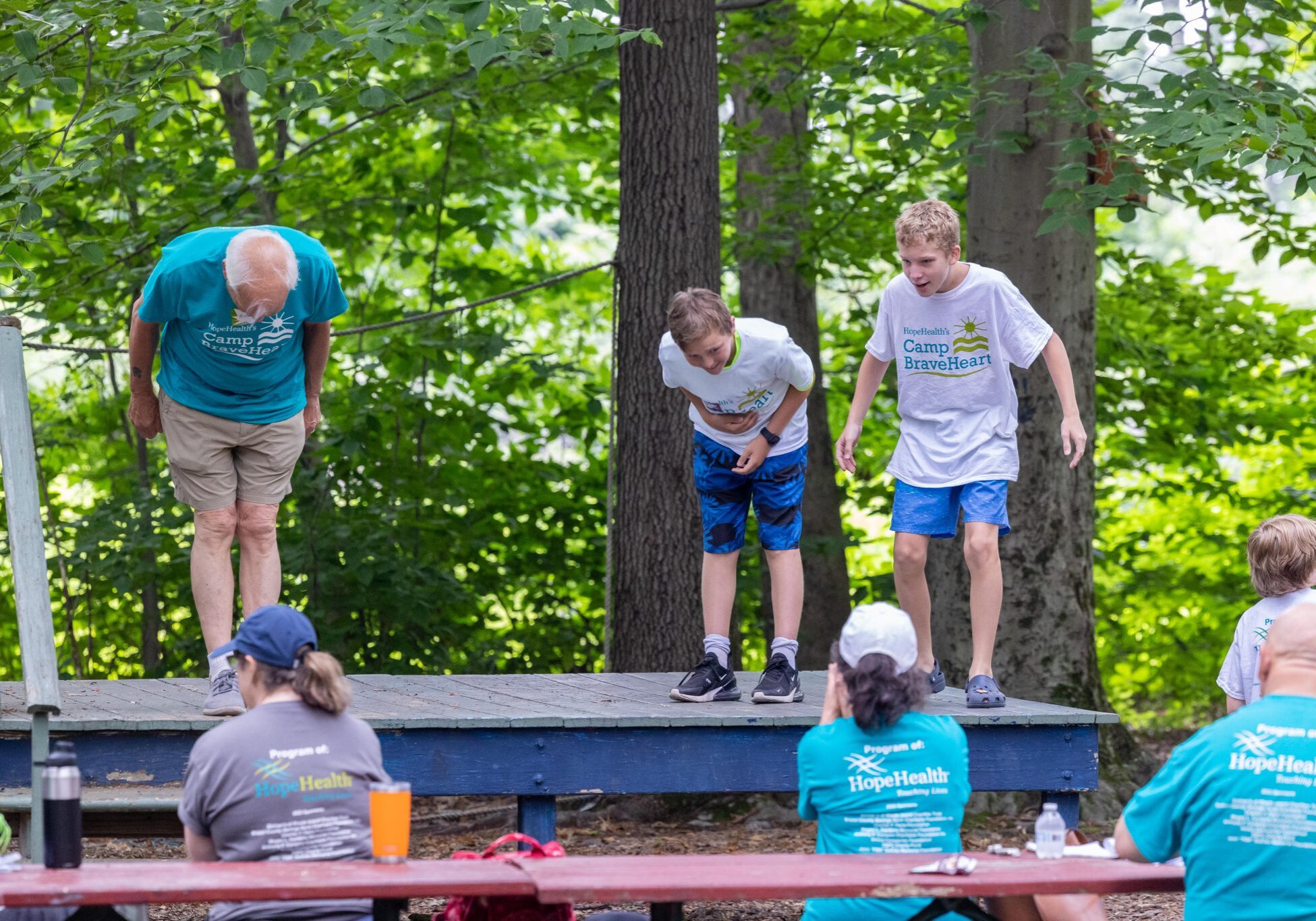 Older man and two boys bow on a theater stage after a performace at Camp BraveHeart, HopeHealth's grief support camp