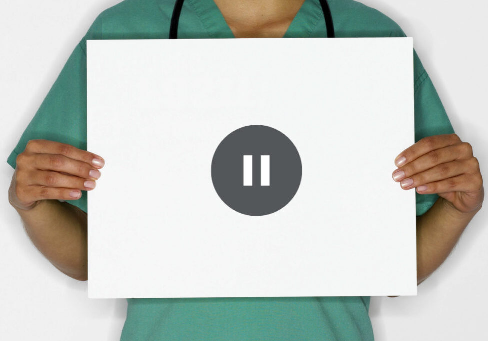 person in scrubs holding sign with pause symbol