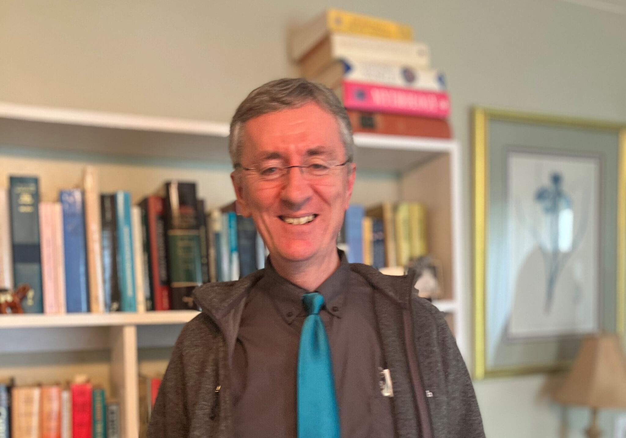 Man wearing teal tie standing in front of a bookshelf