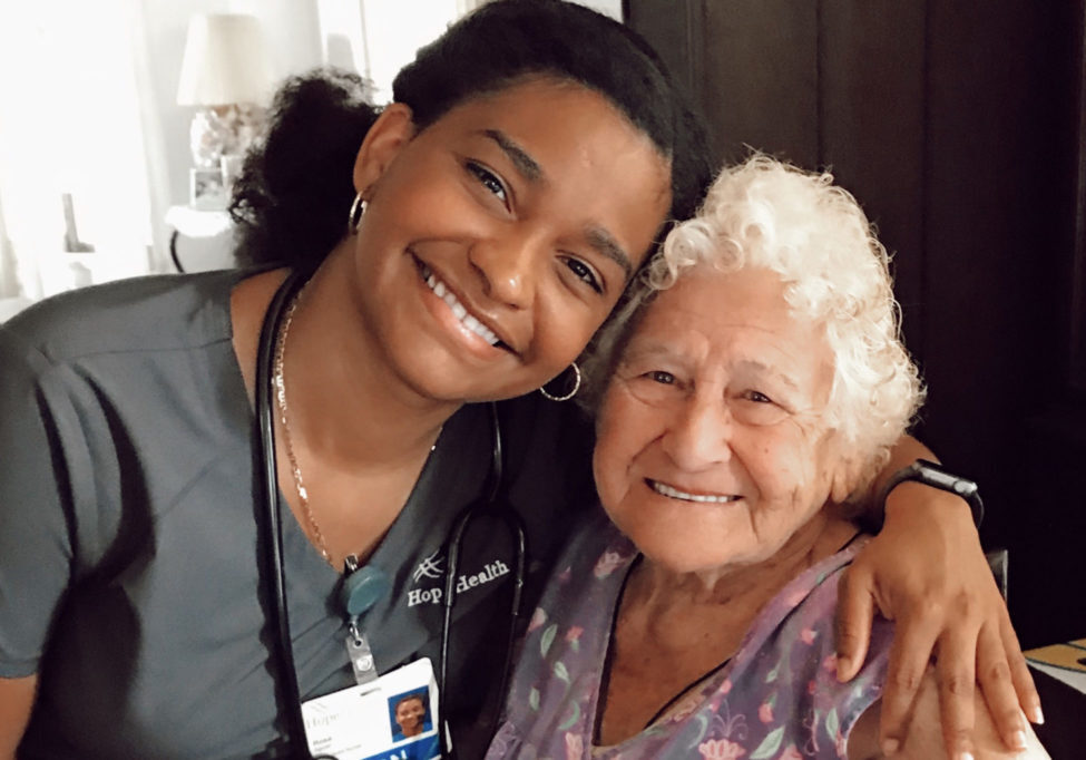 A young nurse wraps her arm around her geriatric female patient