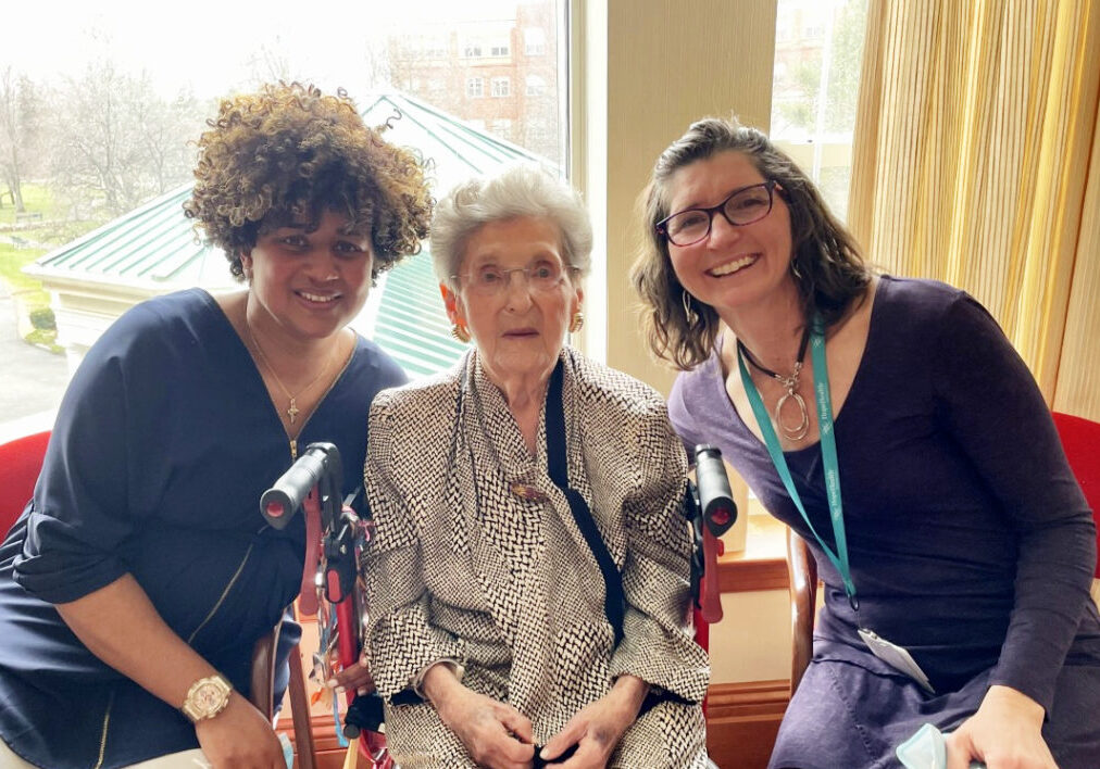 Two young women sit on either side of an elderly woman. The woman on the right is a volunteer who helped the elderly woman finish a legacy project of completing a book