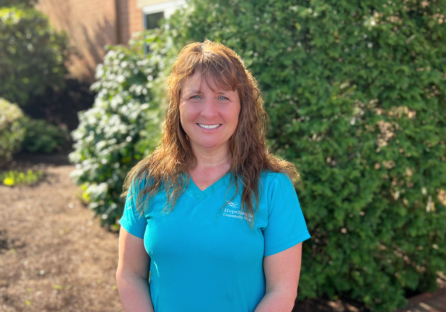 Occupational therapist in teal scrubs standing in a garden surrounded by greenery