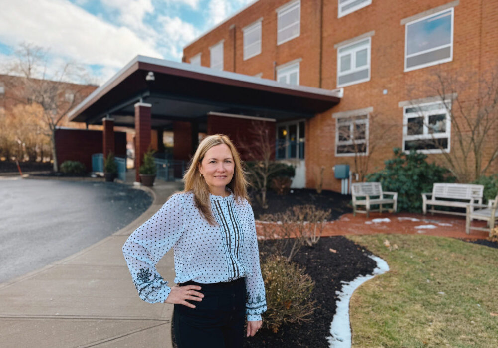 Female pharmicist standing in front of brick Hulitar Hospice Center in Providence, RI