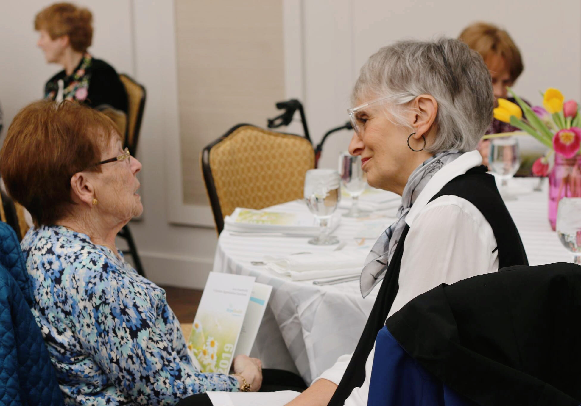 Two older woman sitting at a table speaking compassionately together