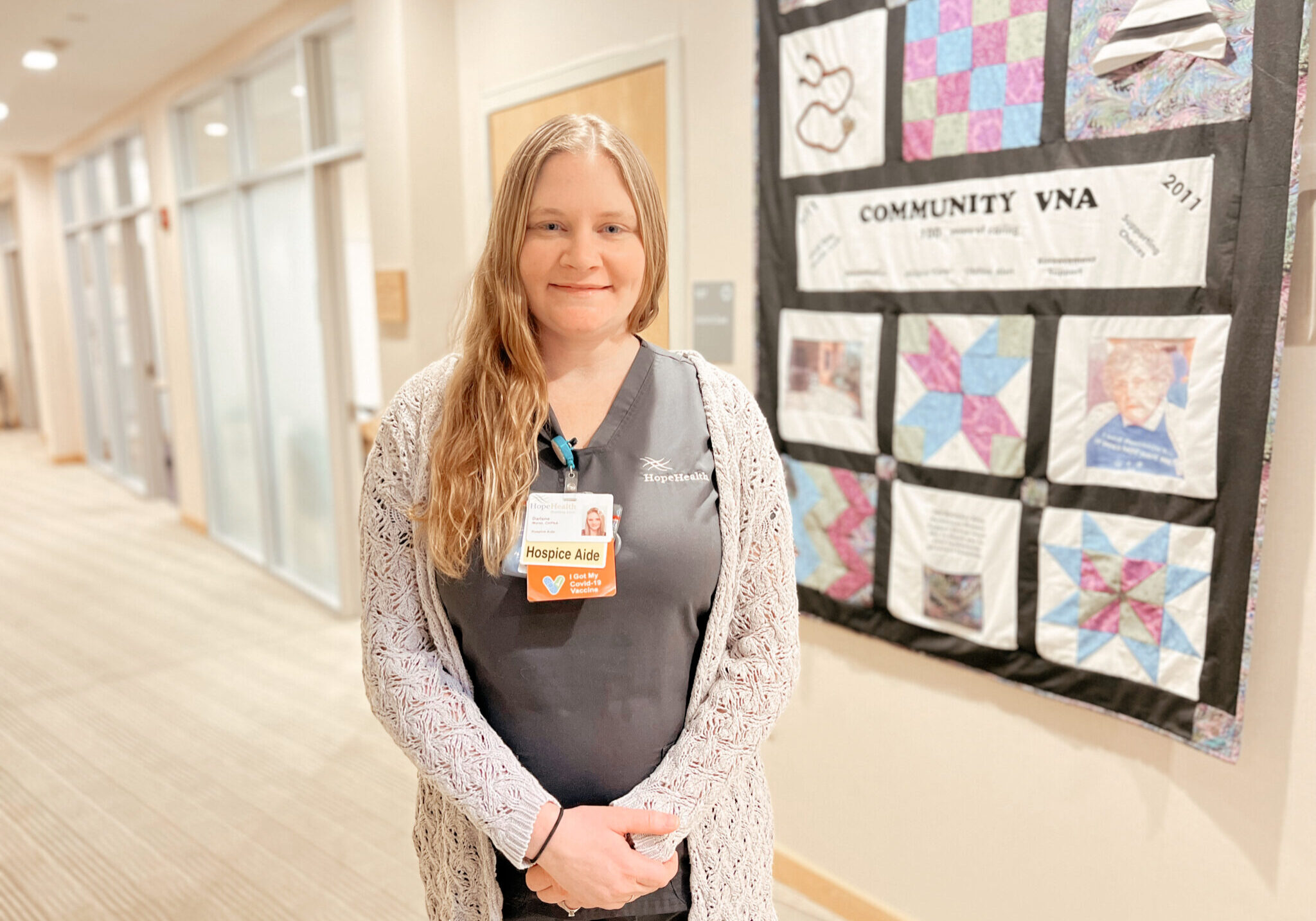 Female hospice aide smiling in front of a commemorative quilt