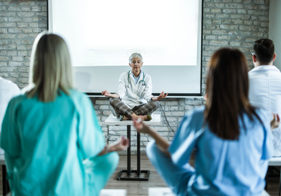 Mature female doctor leading Yoga class in a board room.