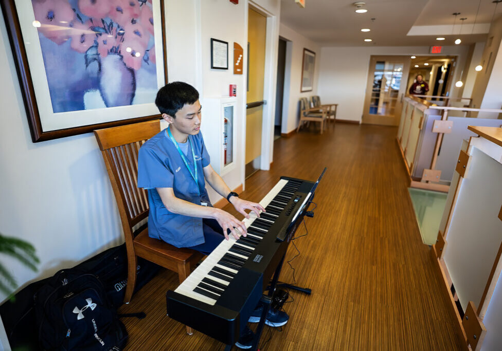 young musician volunteer sits at keyboard at the Hulitar Hospice Center playing music for patients and families