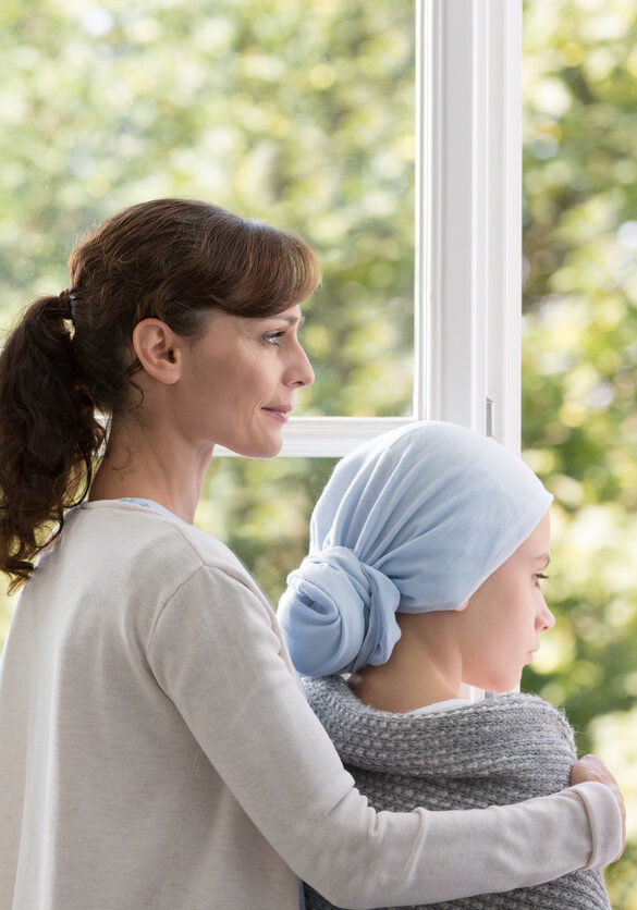 Mother and daughter with cancer in hospital, looking through the window in medical center