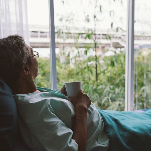 Senior man on a hospital bed alone in a room looking through the hospital window. Elderly patient