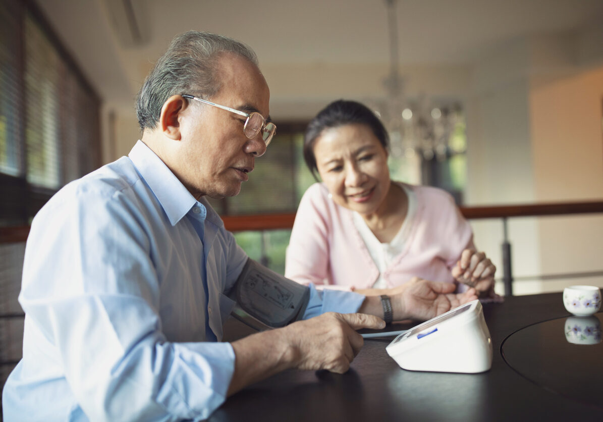 Senior man monitoring his blood pressure at home Senior Asian man monitoring his blood pressure at home and his wife sitting next to him.