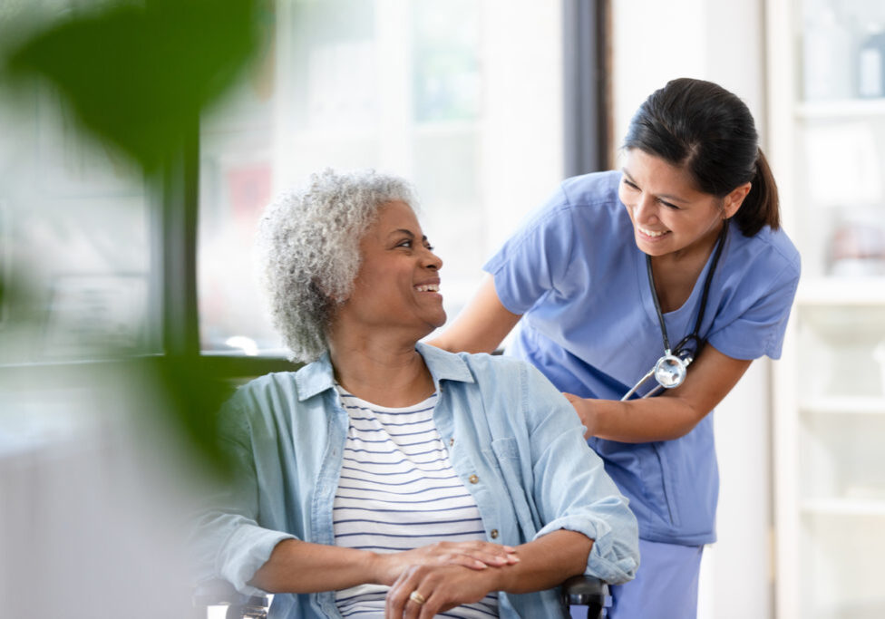 A cheerful female nurse wheels the senior woman into the examination room at the doctor's office.