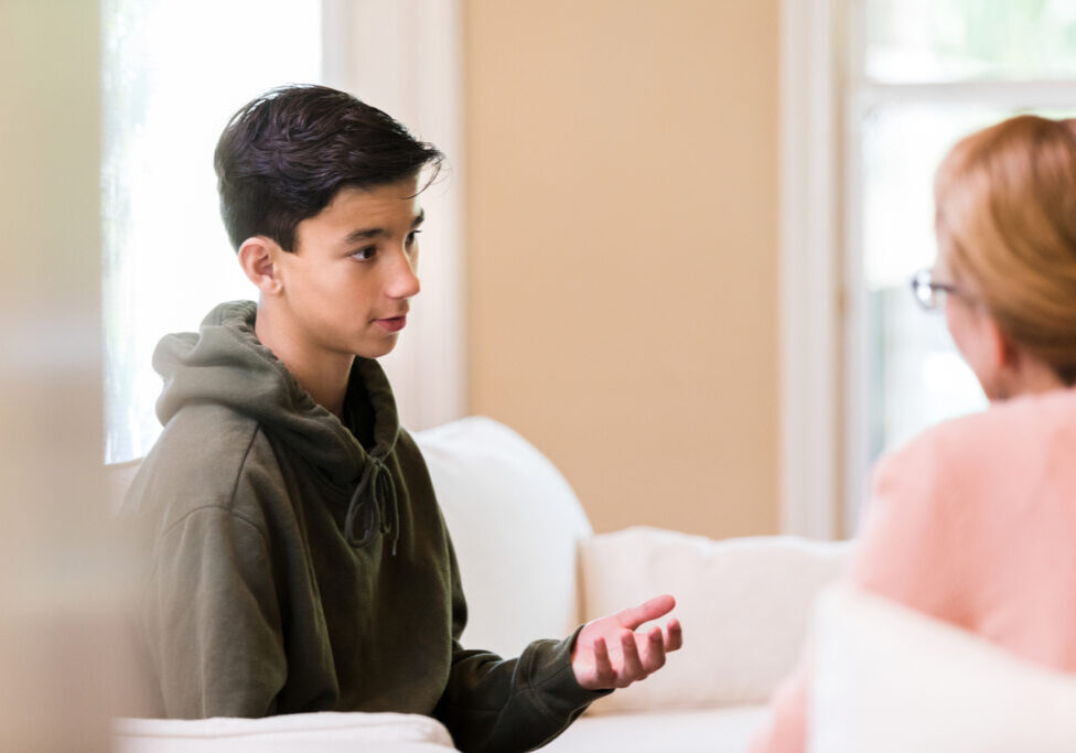 Young preteen boy in a green sweatshirt chats about serious illness and thoughts and concerns about end of life with his mom