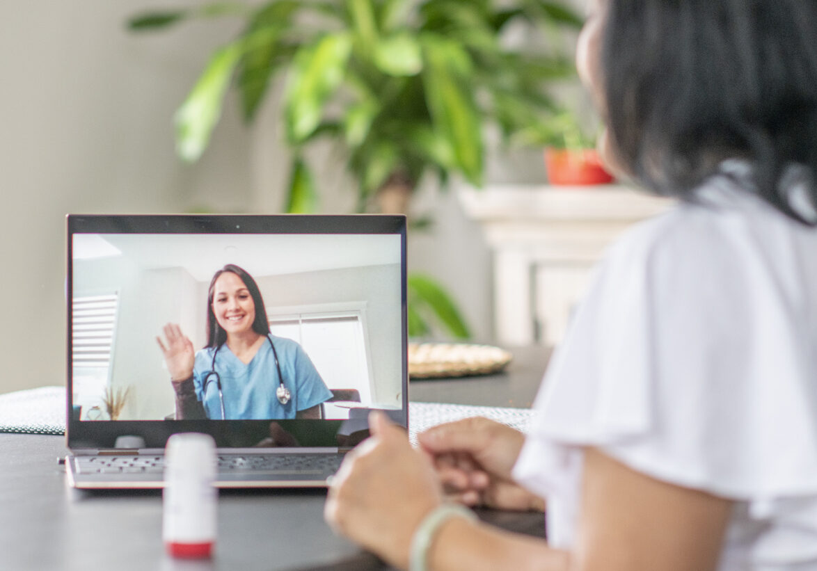 A senior woman sits in her home and discusses with a medical professional via video call on her laptop.