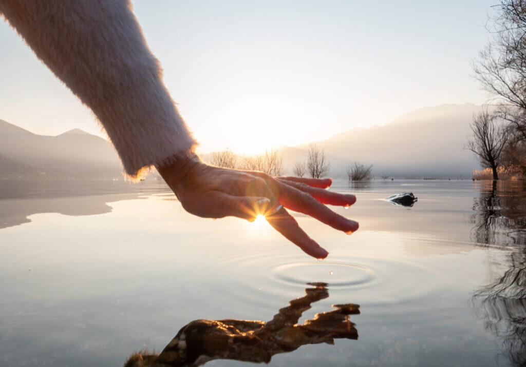 Detail of hand touching water surface of lake at sunset Detail of hand touching and caressing water surface of beautiful lake at sunset, mountain view. Purity freshness clean concept, one person touching lake with hand