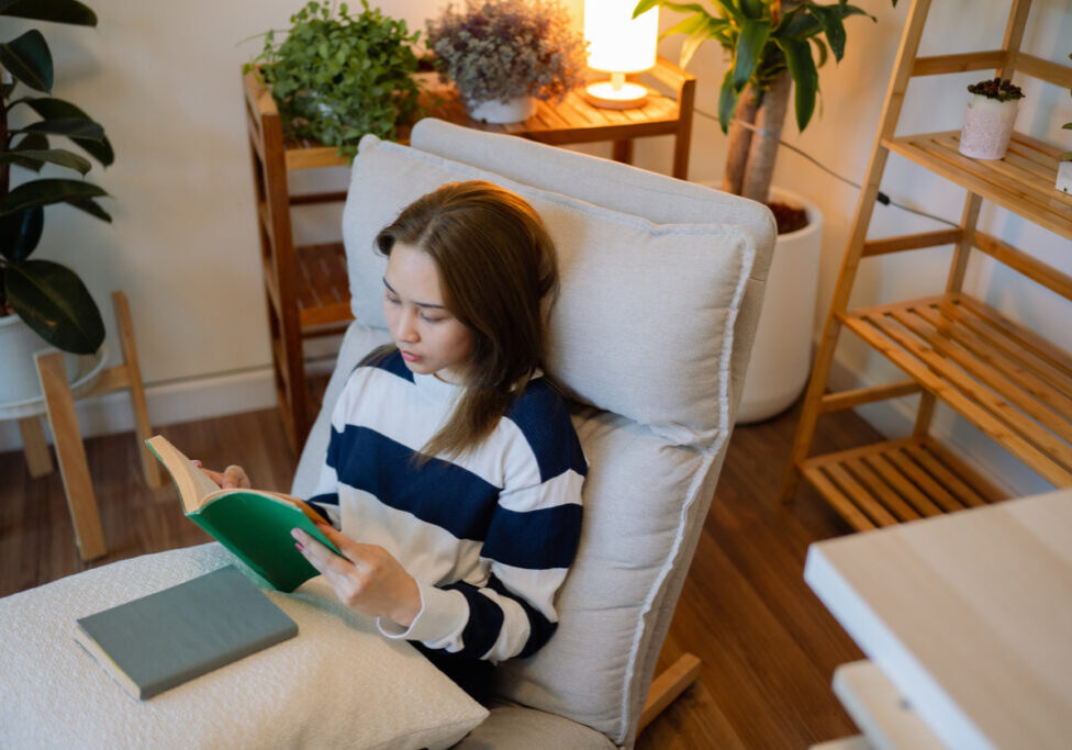 Asian woman reading on the sofa in the evening alone in her living room with the intention and joy of reading.