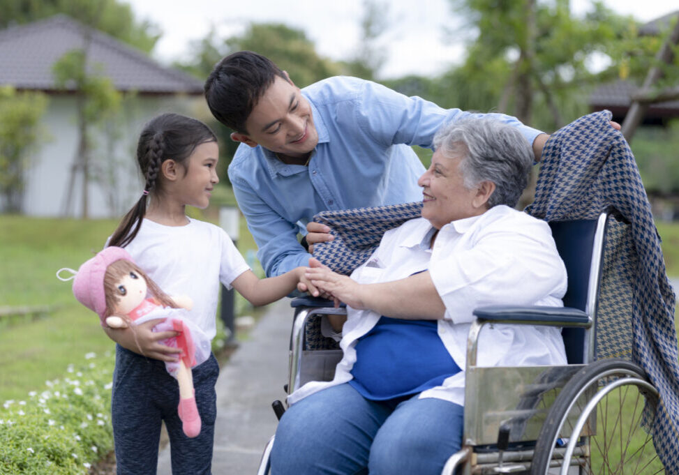 A young man takes a young girl to visit an elderly woman at a nursing home. Asian young man and woman caring for an elderly woman in a wheelchair at a nursing home, a winter-sleeve son warms a middle Eastern mother, a nursing care.