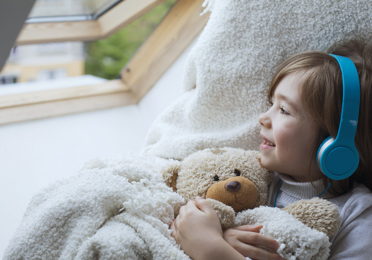 Happy cute boy hugs his teddy bear and listens music at his cozy home.