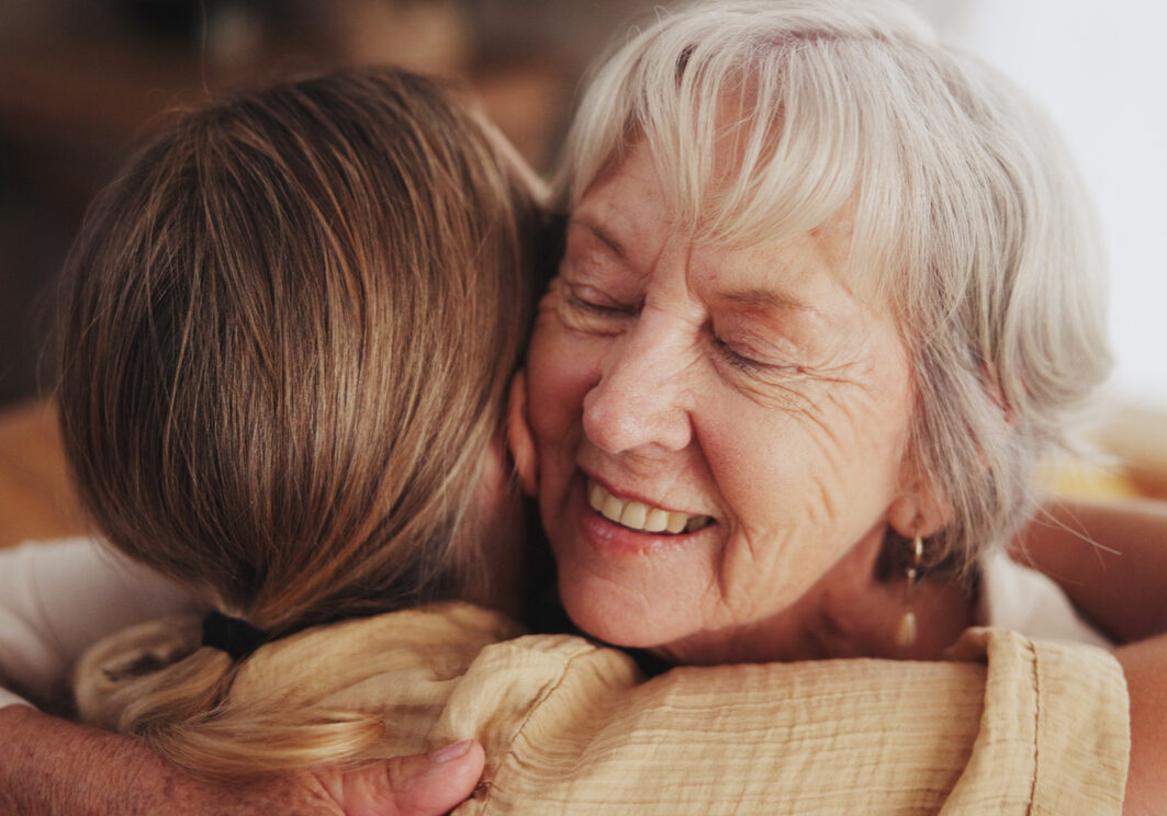 Woman, love and hug senior mom in home for mothers day, bonding and visit in retirement with care or happy. Person, smile and embrace with elderly parent for reunion, comfort and affection in hospice