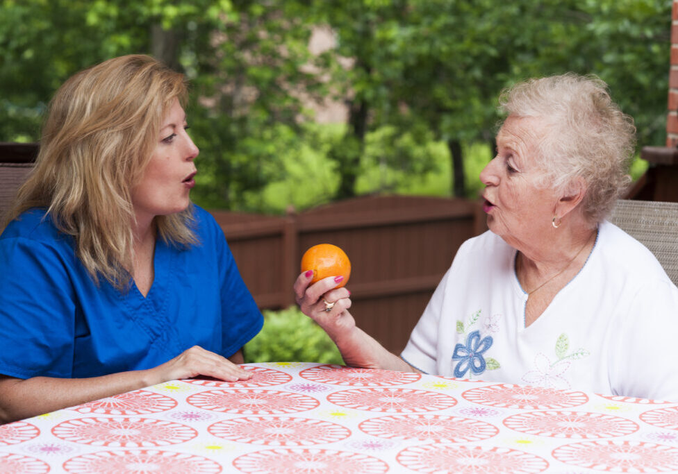 Speech therapist with female stroke patient outdoors during a home health therapy session modeling the production of a consonant during speech training for apraxia