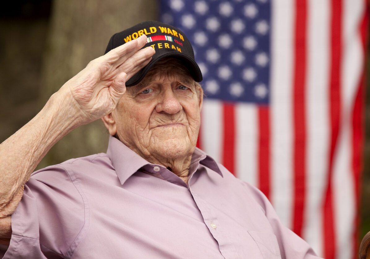 Hand salute and looking directly in to camera with concerned look on his face, with US flag in background. Image shot with Canon 5D Mark2, EF 70-200 f2.8L USM lens, natural light.