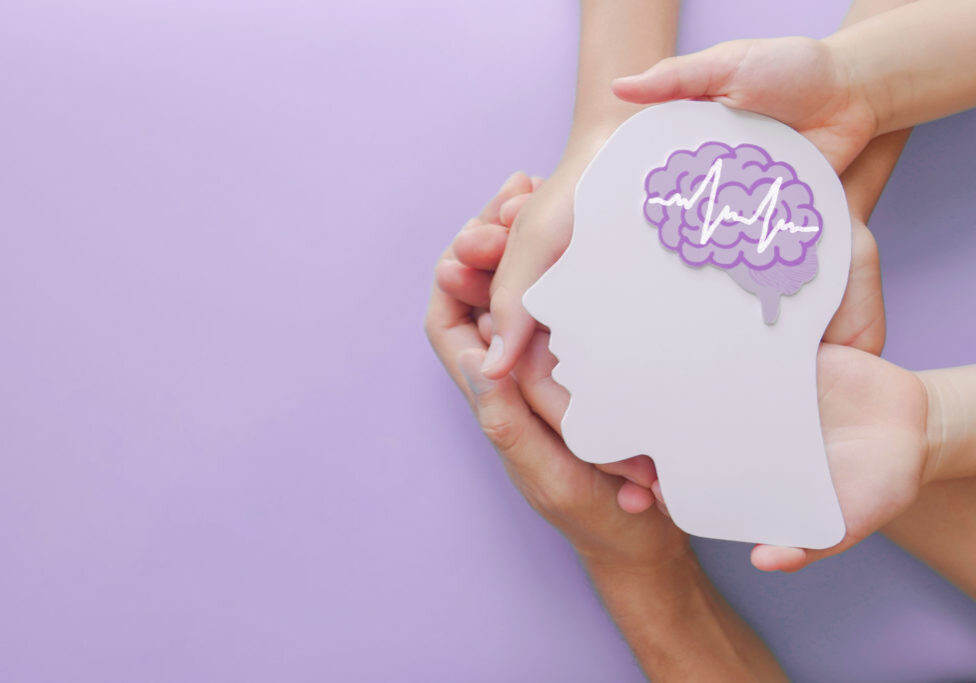 hands hold white cutout head shape with purple brain graphic