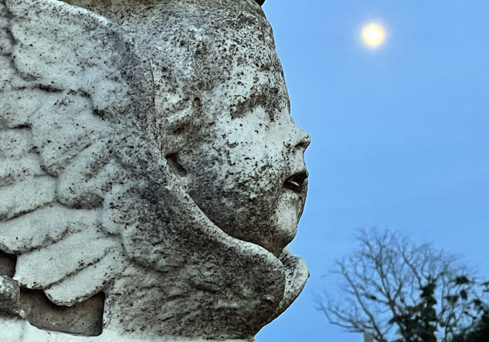 Carved stone cherub looks like it is seeimg the moon in early evening