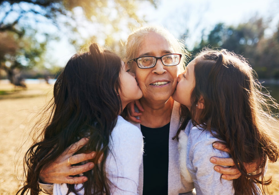 2 girls with long dark hair kiss elderly relative's cheeks