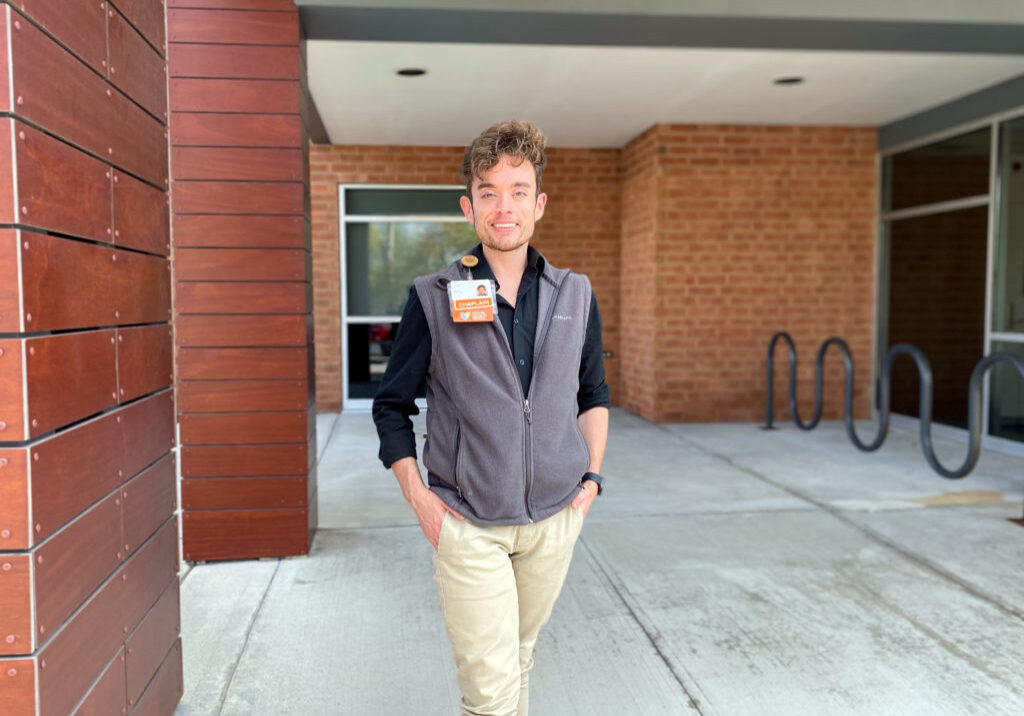 Young man in gray vest standing outside entrance to building